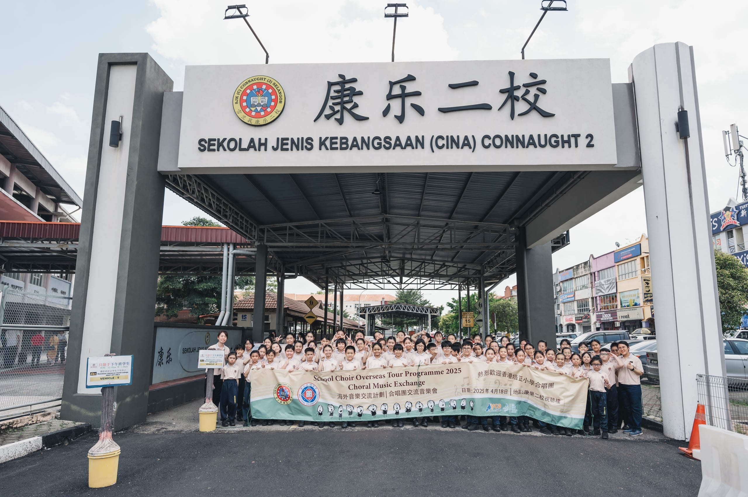 Hong Kong Pui Ching Primary School Choir and their hosts hold a School Choir Overseas Tour Programme 2025 banner at the gate of SJK (C) Connaught 2 primary school, Kuala Lumpur, 18 April 2025